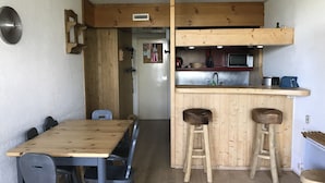 Cocina compacta con detalles de madera, comedor con mesa y sillas, y un taburete de bar.