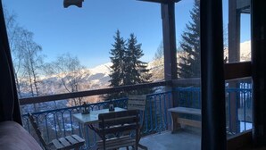 Un balcón con vistas a montañas nevadas, una mesa de madera y un banco.