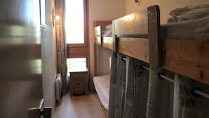 Una habitación pequeña con una cama litera de madera, una mesita de noche y una ventana con cortinas.
