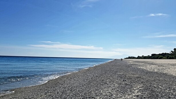 A pebbled beach with a clear sky and calm sea.
