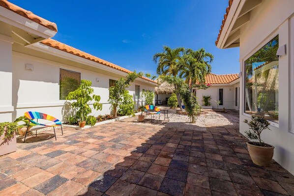 A courtyard with a tiled floor, potted plants, and outdoor furniture. - Colonial Modern Villa Sleep 14-Pool, Palapa, Court (Noord)