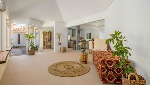 A spacious living room with a large sofa, a round woven rug, and several potted plants. - Colonial Modern Villa Sleep 14-Pool, Palapa, Court (Noord)