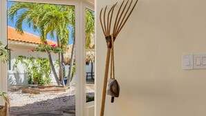 A room with a woven ottoman, a rustic rake, and a view of a beach with palm trees. - Colonial Modern Villa Sleep 14-Pool, Palapa, Court (Noord)