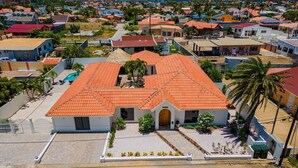 An aerial view of a residential area with a prominent house featuring a red-tiled roof, a front entrance, and a small garden area. - Colonial Modern Villa Sleep 14-Pool, Palapa, Court (Noord)