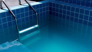 Una piscina con borde de azulejos y escalera metálica.