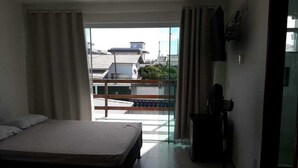 Habitación de hotel con cama, una mesita, televisor y balcón con vista a edificios.