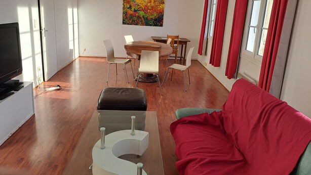 Ein modernes Wohnzimmer mit einem Holzes Esstisch, weißen Stühlen, einem roten Sofa und einem Glastisch.