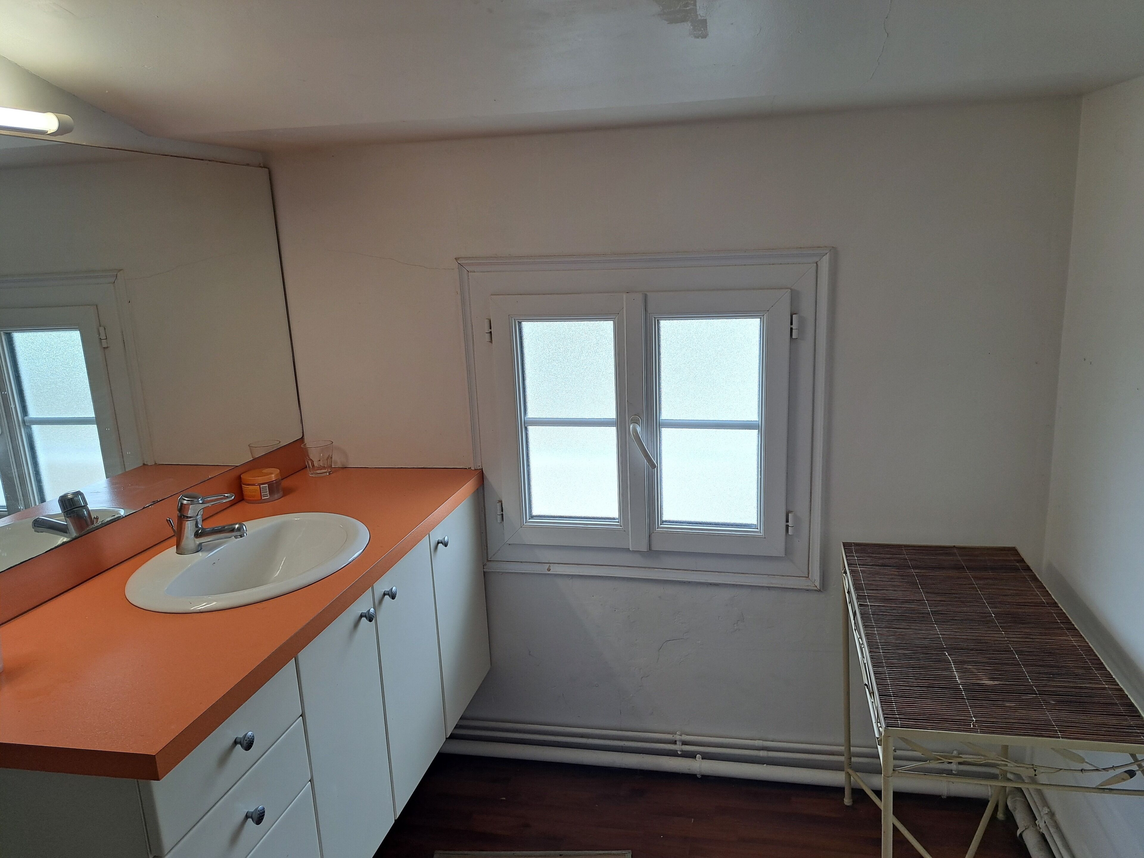 A small bathroom with a white sink, a mirror, and a window.