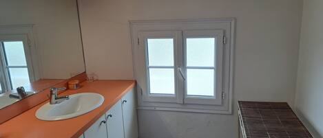 A small bathroom with a white sink, a mirror, and a window.