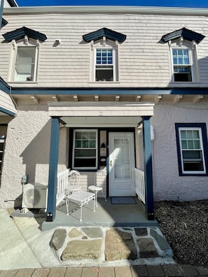 Stylish two-story home with a central entrance, two upper-floor windows, and a cozy outdoor seating area.