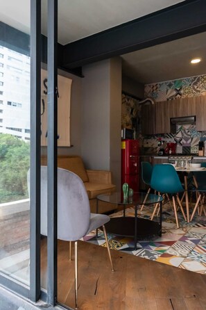 A modern living space with a glass partition, a sofa, a dining table with chairs, and a kitchen area with patterned tiles.