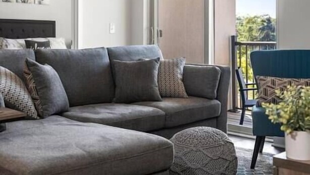 Un salon moderne avec un canapé d’angle gris, un pouf rond et un tapis à motifs.