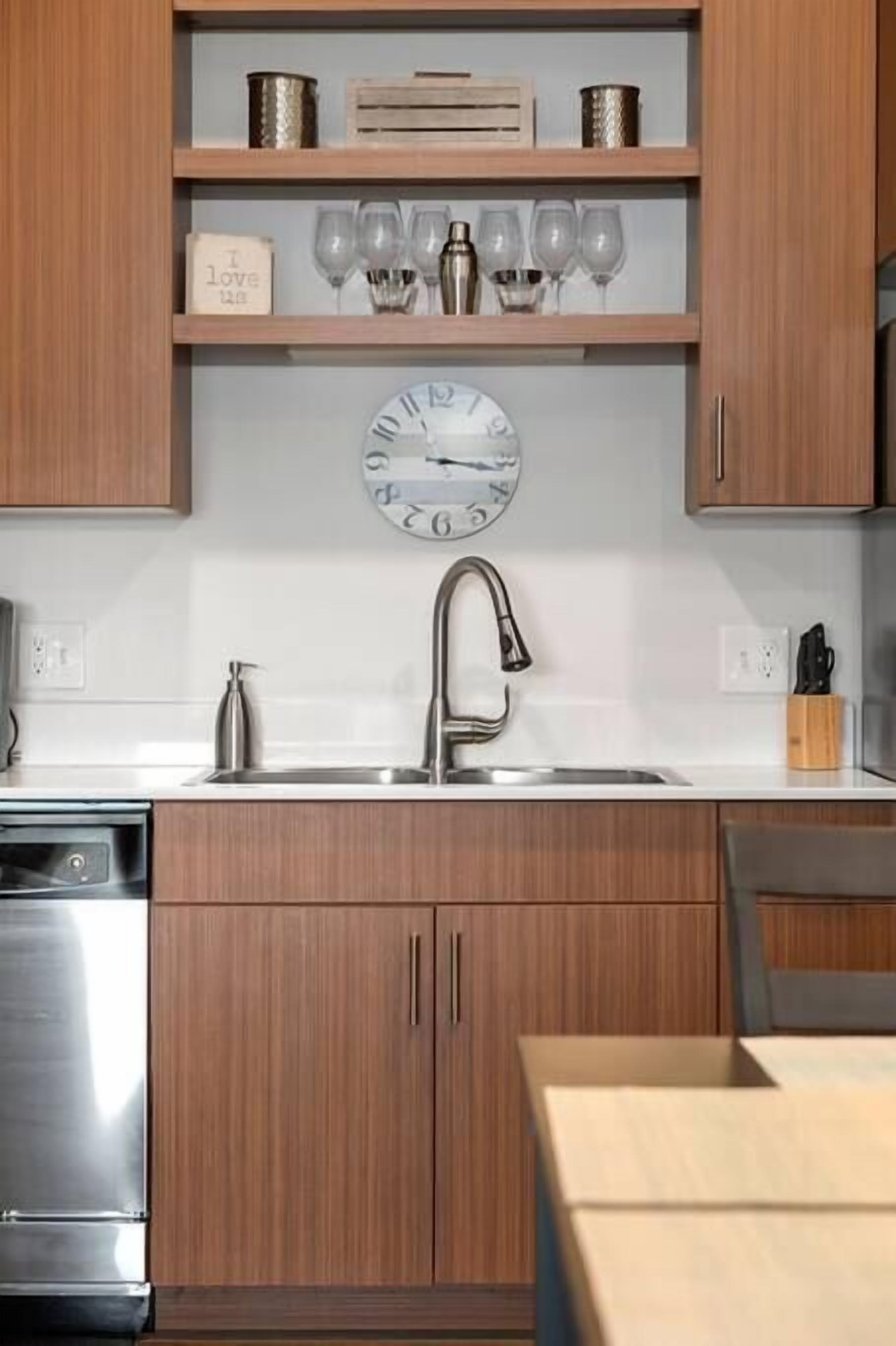 A modern kitchen with wooden cabinets, a stainless steel sink, and a clock above the countertop.