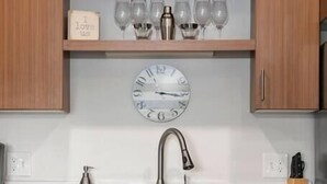 Une cuisine moderne avec des meubles en bois, un évier en acier inoxydable et une horloge au-dessus du plan de travail.