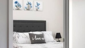 Une chambre à coucher avec un lit, une table de chevet et une lampe. Trois œuvres d’art sont accrochées au mur au-dessus du lit.
