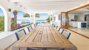 Un vaste espace extérieur aménagé pour les repas, avec vue sur la mer, une cuisine moderne et une piscine.