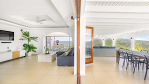 A spacious living area with a sofa, dining table, and chairs, a kitchen area, and a view of the outdoors.