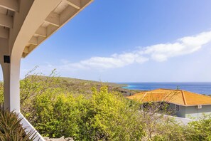 A coastal property with a view of the ocean, a tiled roof, and surrounding greenery.