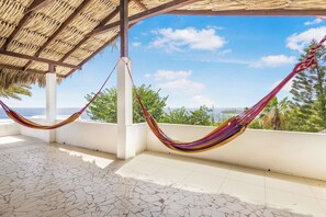 A hammock under a thatched roof, a tiled floor, and a view of the sea.