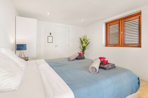 A bedroom with two beds, a bedside table with a lamp, a door, and a window with shutters.