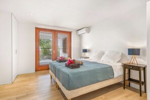 Ein Schlafzimmer mit einem Bett, Nachttischen, einer Lampe und einem Fenster mit Jalousien.