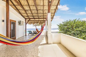 Un espacio al aire libre techado con una hamaca, sillones de descanso y vista al mar.