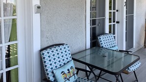 Ein überdachter Patio-Bereich mit einem Glastisch und zwei Stühlen, jeweils mit gemusterten Kissen.