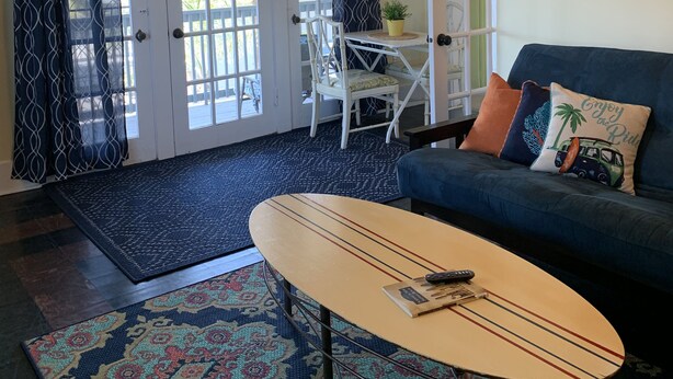 Ein Wohnzimmer mit blauem Sofa, Couchtisch, Teppich mit Muster, Deckenventilator und einer mit Vorhängen versehenen Tür.