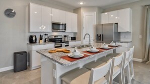 A modern kitchen with white cabinetry, a central island with seating, stainless steel appliances, and a clock on the wall. - Super spacious villa private pool, themed beds (Kissimmee)