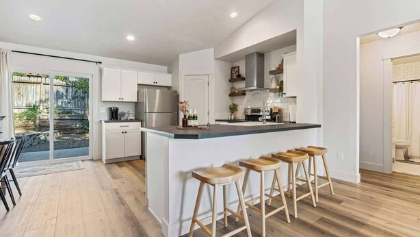 A modern kitchen with a central island, bar stools, and a sliding glass door leading to a patio. - Nampa Greenbelt Retreat | Hot Tub | Walk to Indian Creek | Sleeps 10 (Nampa)