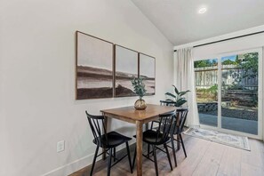 Un coin repas avec une table en bois et des chaises noires, un vase avec une plante et trois œuvres d’art encadrées accrochées au mur.