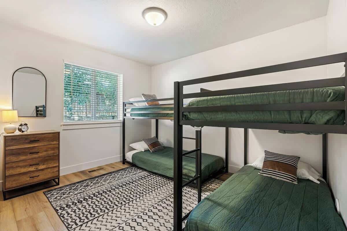 Une chambre avec des lits superposés, une commode, un tapis à motifs et une fenêtre avec des stores.