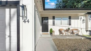 A modern house with a garage door, a number '44' on the wall, a covered porch with outdoor furniture, and a small garden area. - Nampa Greenbelt Retreat | Hot Tub | Walk to Indian Creek | Sleeps 10 (Nampa)