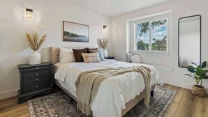 A bedroom with a bed, bedside tables, a window with blinds, a mirror, and a potted plant. - Nampa Greenbelt Retreat | Hot Tub | Walk to Indian Creek | Sleeps 10 (Nampa)