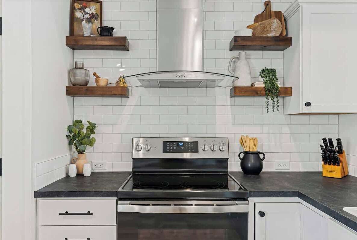 A modern kitchen with white cabinetry, a stainless steel stove, and wooden shelves with decorative items.