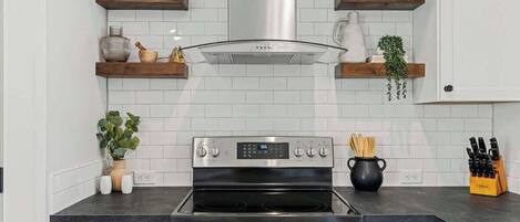 A modern kitchen with white cabinetry, a stainless steel stove, and wooden shelves with decorative items.