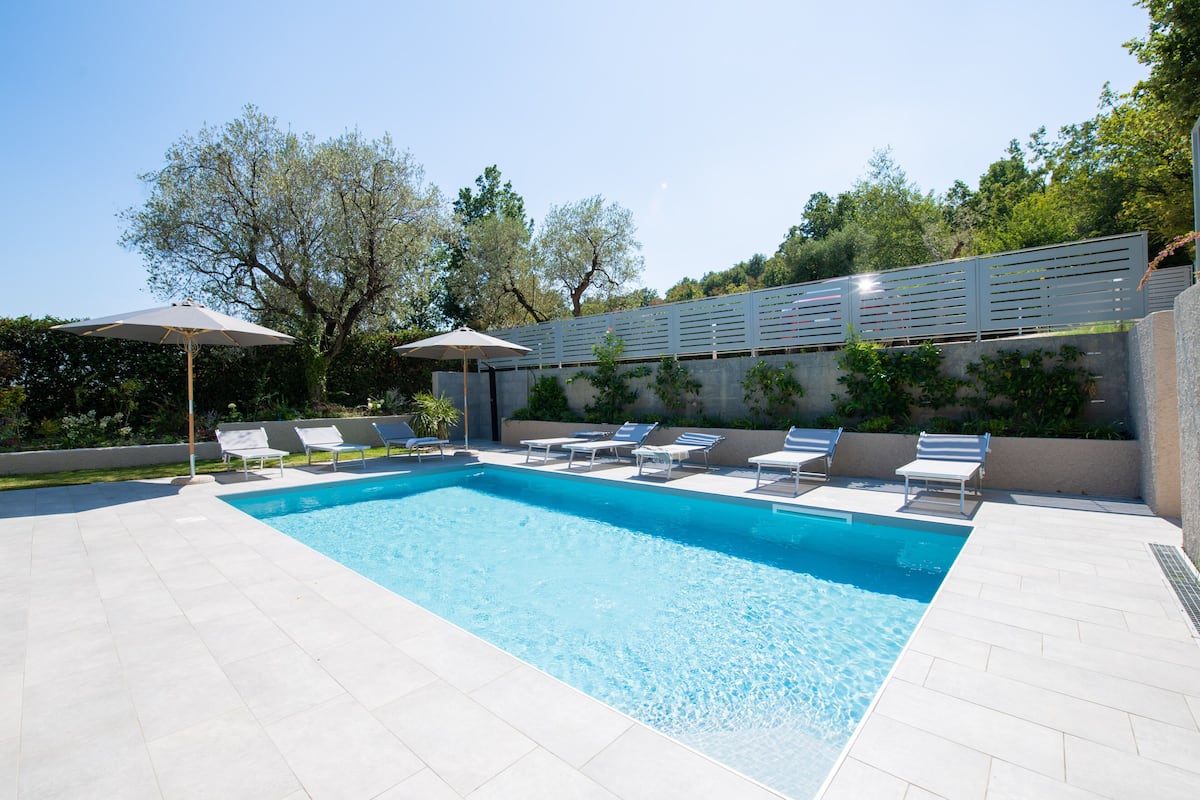 Une piscine rectangulaire dont le fond est recouvert de carreaux blancs, entour ée de chaises longues blanches et de parasols.