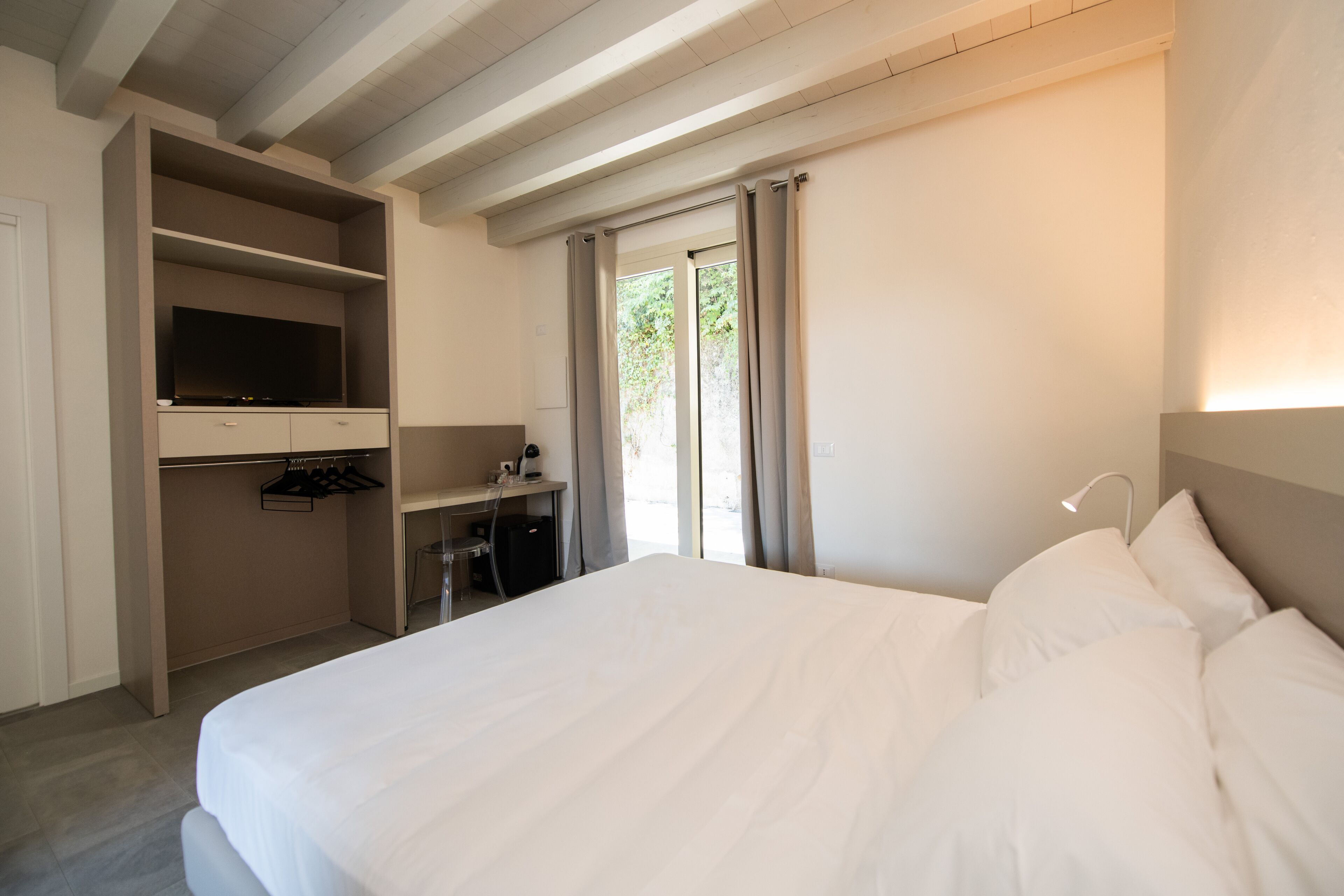 A hotel room with a bed, a desk with a television, and a window with curtains.