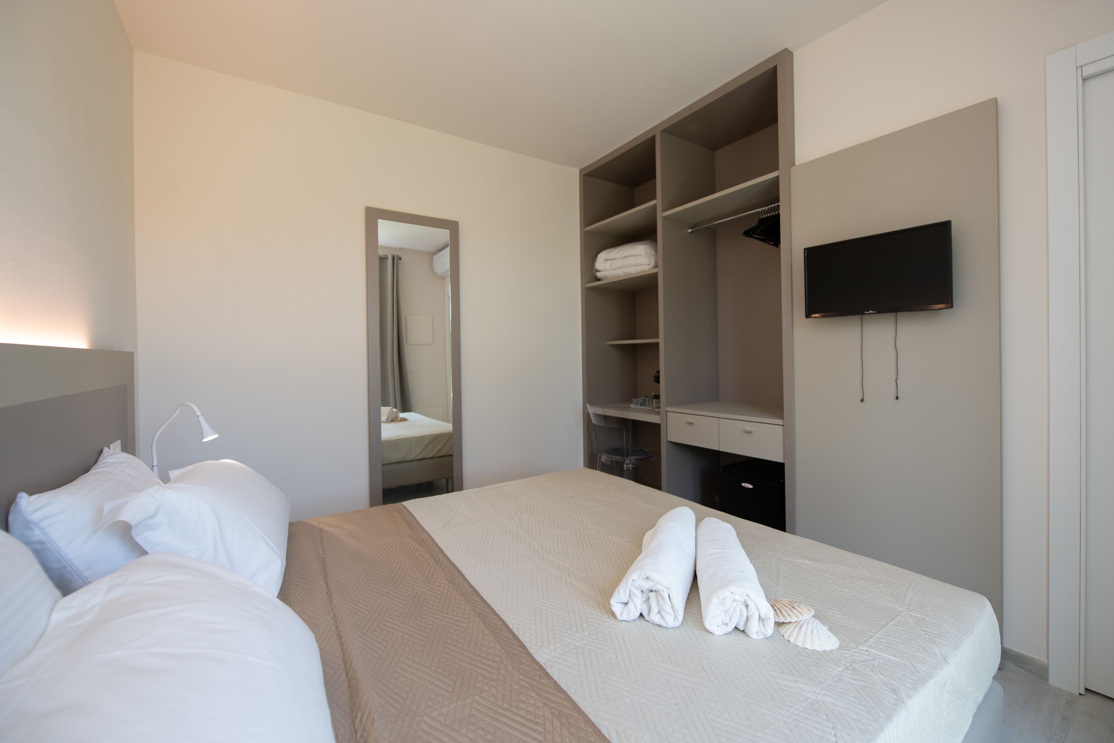 Una habitación de hotel con una cama, un espejo grande, un armario y un televisor.