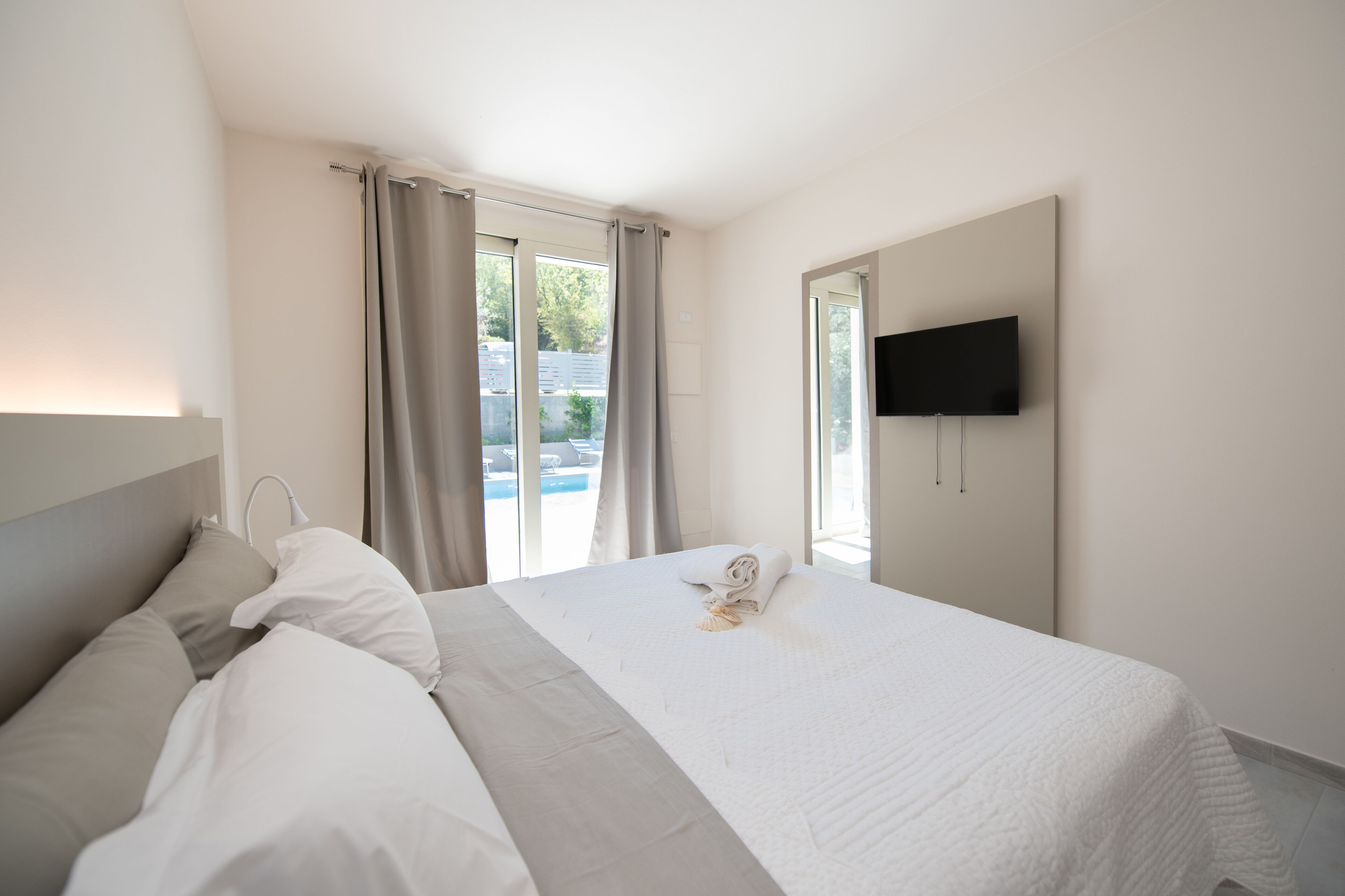 Una habitación de hotel con cama, televisor montado en la pared y ventana con cortinas.