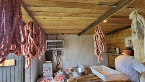 A meat processing area with hanging sausages, a meat grinder, and a person working. - Comfortable guest rooms. (Yviers)