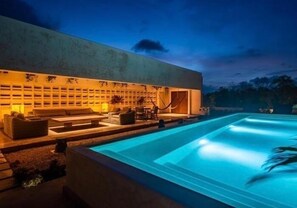 Un espace piscine extérieur moderne, doté d’un coin salon et d’une grande fontaine.