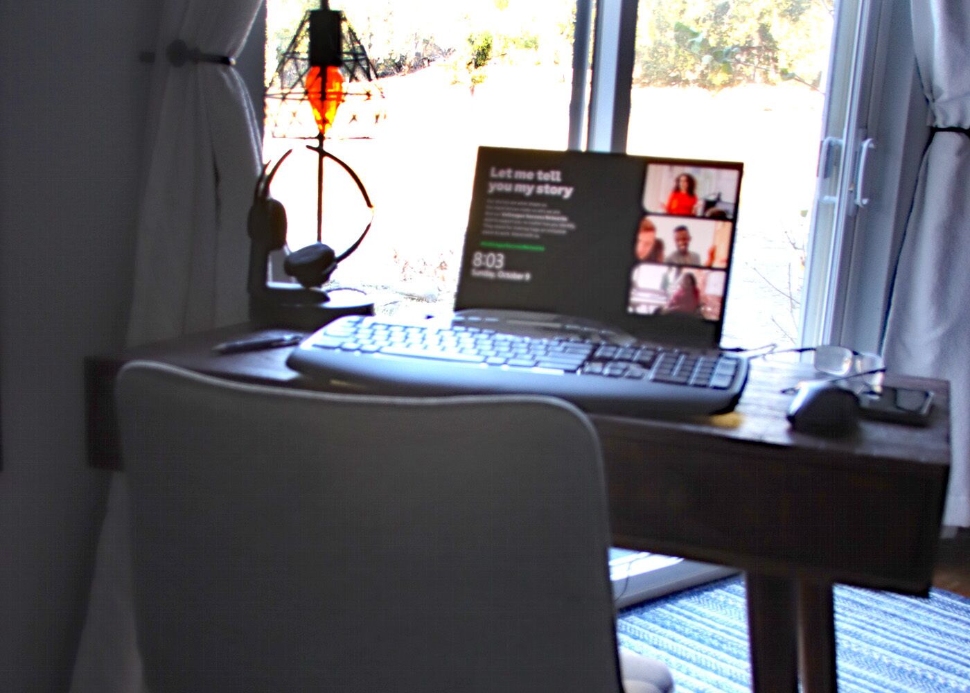 A laptop on a desk with a keyboard and mouse, a microphone, and a screen displaying a video call interface.