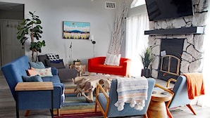 A living room with a blue sofa, red armchair, and a stone fireplace. There is a painting on the wall and a plant in the corner. - Private Home at the foot of Yosemite National Park (Mariposa)