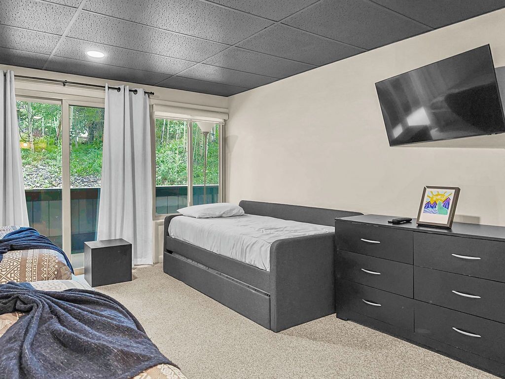 A bedroom with a bed, a dresser, a TV, and a window with curtains.