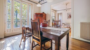 A dining area with a wooden table and chairs, a large window with a view of trees, and a radiator on the wall. - Large 1BR close to Bastille and Aligre (Paris)