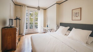 A hotel room with a bed, a desk, a chair, a dresser, and a window with curtains. - Large 1BR close to Bastille and Aligre (Paris)