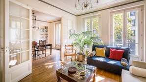 A spacious living room with a dark blue sofa, a glass coffee table, and a dining area with wooden chairs and a table. - Large 1BR close to Bastille and Aligre (Paris)