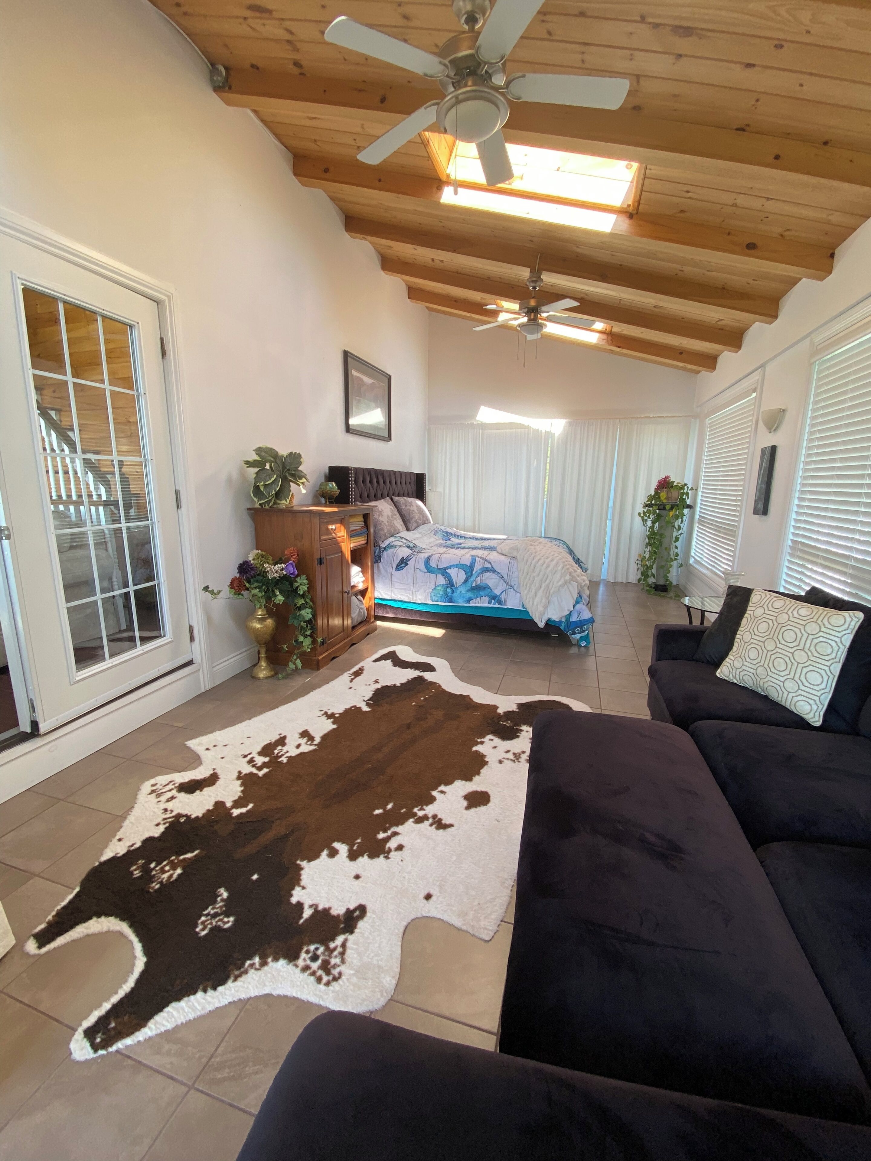 A spacious living room with a cowhide rug, a dark sofa, and a ceiling fan.