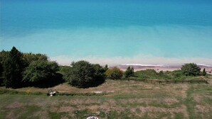 Un paisaje costero con vista despejada al mar, una zona con césped y una valla, y algunos árboles.